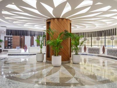 Moderne Hotellobby mit rundem Marmorboden, Pflanzen und elegantem Empfangstresen.