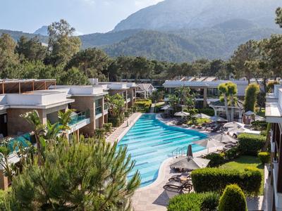 Moderner Hotelkomplex mit einem großen Pool, umgeben von Bergen und grünen Gärten.