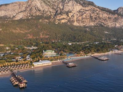 Luftaufnahme eines Hotels mit Pool und Bootsanlegern an der Küste vor hohen Bergen.