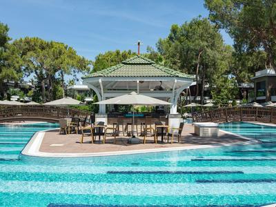 Poollandschaft mit blauem Wasser und überdachter Sitzgelegenheit in einem Hotelgarten.