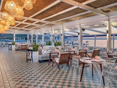 Offenes Hotelrestaurant mit modernen Möbeln und Blick auf das Meer bei Sonnenuntergang.