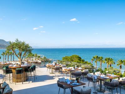 Offene Restaurantterrasse mit Blick auf das Meer, Palmen und blauem Himmel.