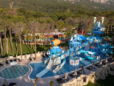 Freizeitpark mit großen blauen Wasserrutschen, Pools und Liegestühlen in einer bewaldeten Umgebung.