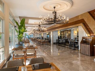 Heller Hotel-Speisesaal mit großen Fenstern, Holzstühlen und modernen Kronleuchtern.