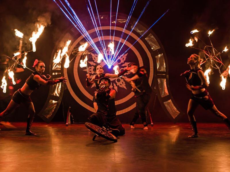 Dancers with torches and colorful lasers on stage in front of a large target.