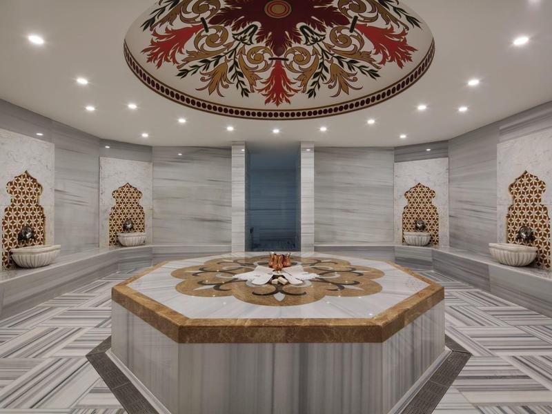 Elegant Turkish hammam with central marble washing basin and decorated walls.