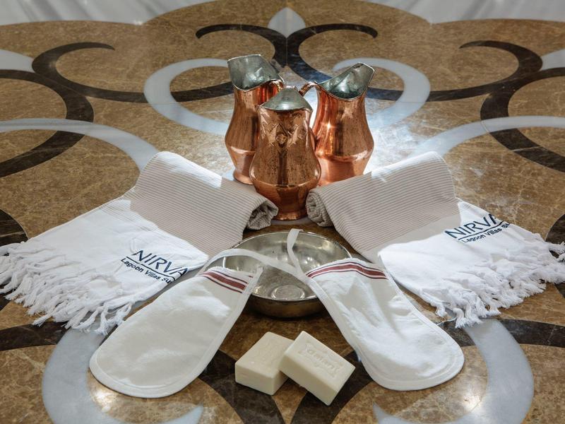 Hotel set with bathrobe, slippers, soap, and copper pitchers on decorative floor.