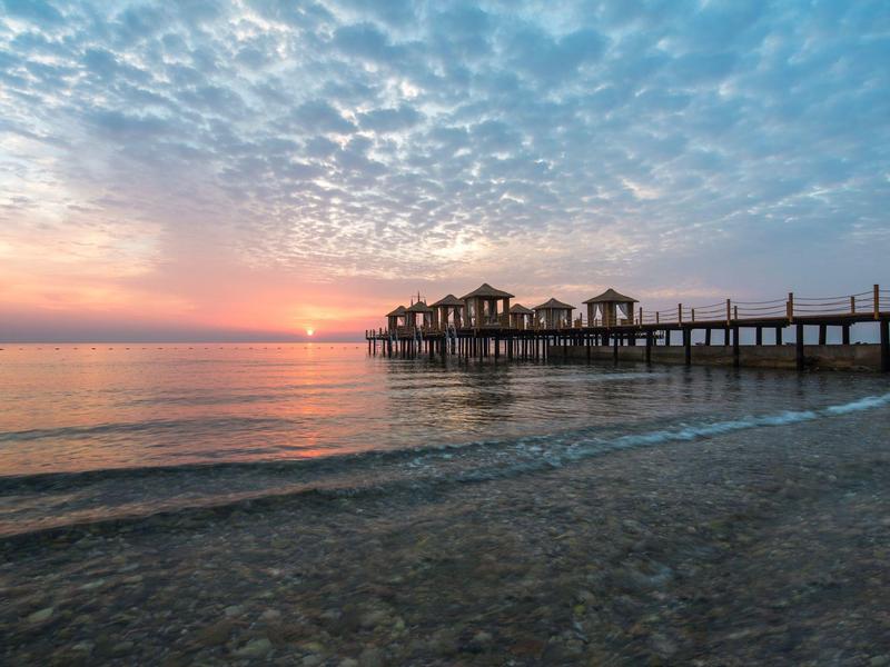 Pier with small huts over calm sea at sunset with cloudy sky.