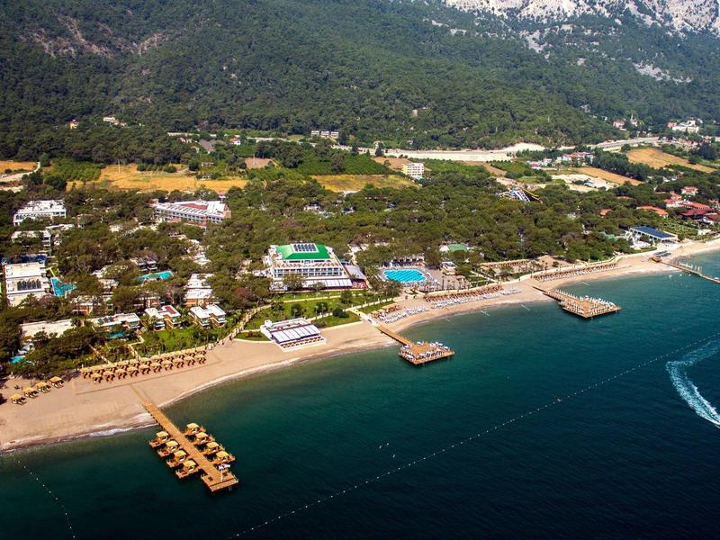 Aerial view of a beach with resorts, docks, and forested mountains in the background.