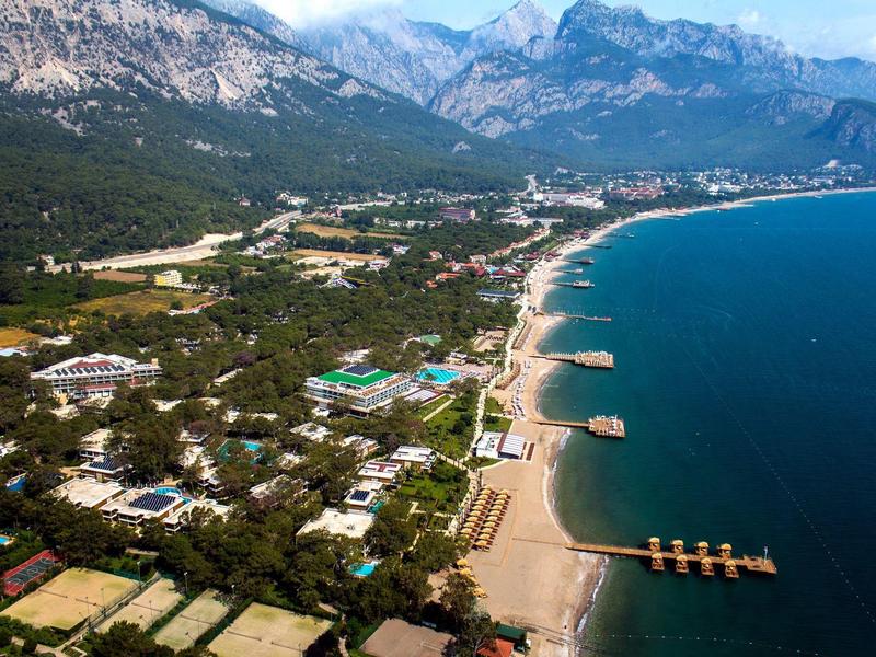 Aerial view of a coastal town with beach, buildings, and mountains in the background.