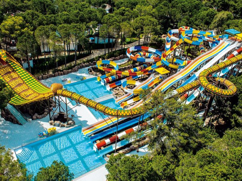 Colorful water park with multiple slides and pools surrounded by lush greenery.