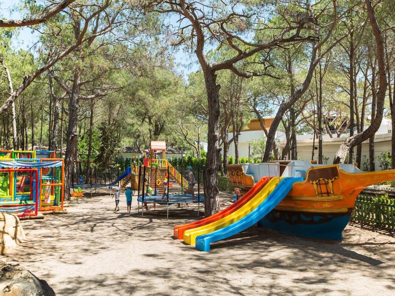 Colorful children's playground with slides and climbing equipment in wooded area near hotel.