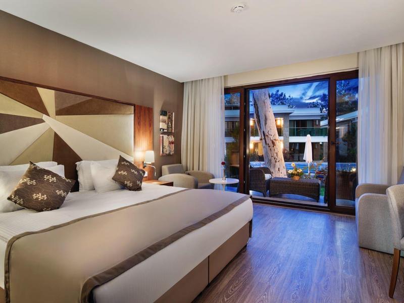 Modern hotel room with large double bed and terrace overlooking the pool.