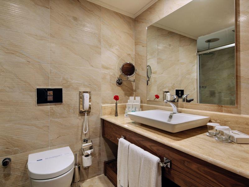 Modern hotel bathroom with toilet, sink, large mirror, and towels.
