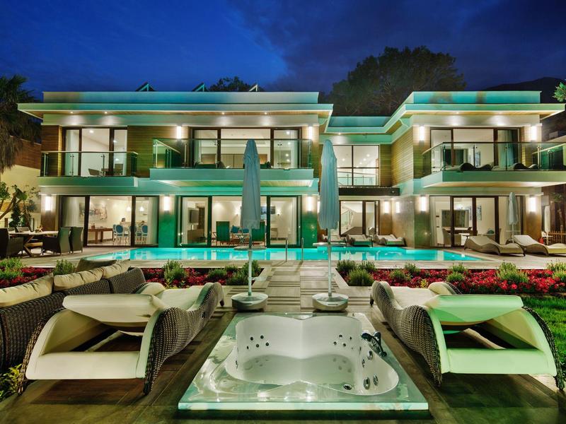 Luxurious modern villa with illuminated pool and hot tub in garden at night.