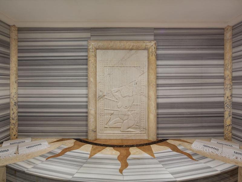 Modern massage room with wooden benches, striped wall paneling, and integrated stone relief.