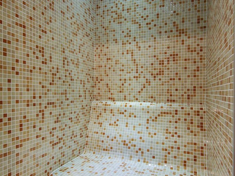 Sauna room with bench and small colorful mosaic tiles on walls and bench.