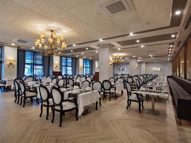 Elegant hotel restaurant with white tablecloths, black chairs, and chandeliers on the ceiling.