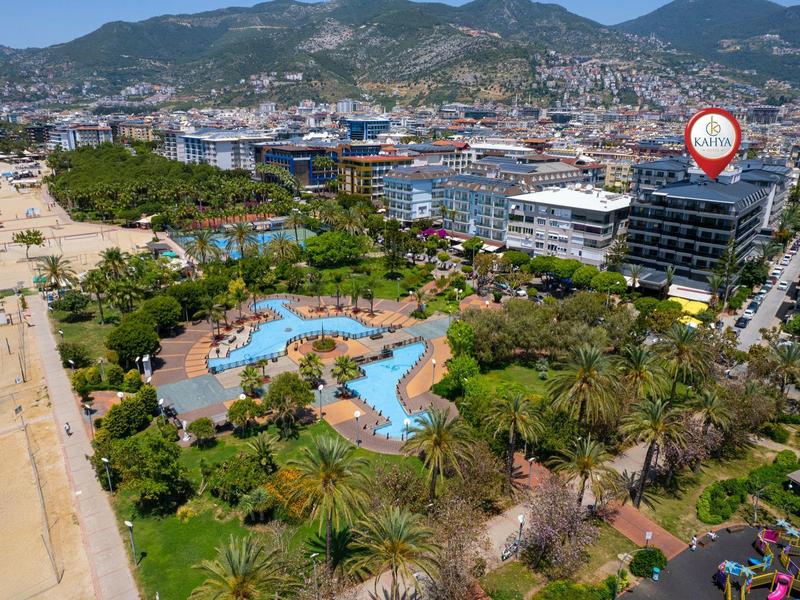 View of a hotel garden with pool, palm trees, and beaches in front of mountains