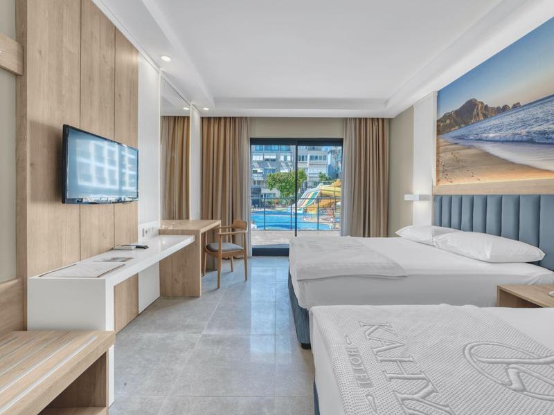 Bright hotel room with two beds and a view of the pool through a glass door.