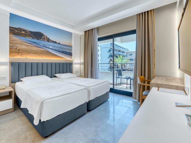Bright hotel room with two single beds, balcony, and large landscape picture on the wall.