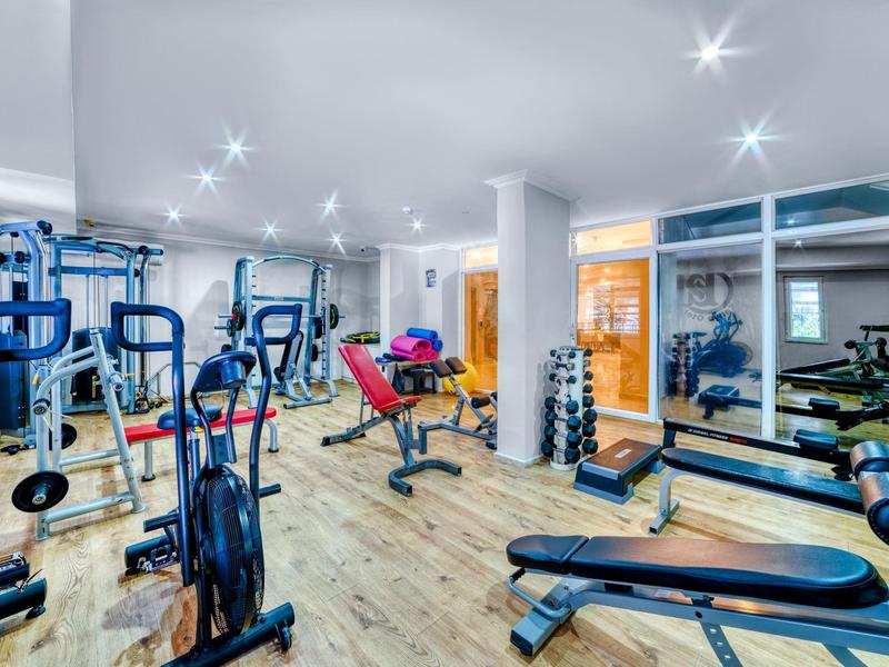 Bright gym with various workout equipment and mirrored wall.