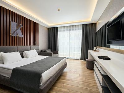 Modernes Hotelzimmer mit Doppelbett, Sofa, TV und großem Fenster mit Vorhängen.