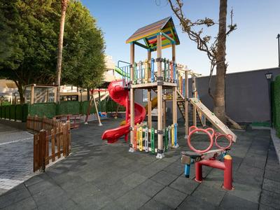 Kinderspielplatz mit Rutsche und Schaukel in einem Außenbereich neben einem Hotel.