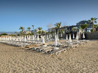 Leere Liegen und geschlossene Sonnenschirme am Sandstrand vor einem Hotelgebäude