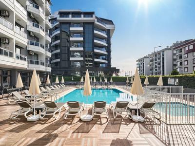 Moderner Hotelpool mit Liegestühlen und Sonnenschirmen auf einer Terrasse zwischen Wohngebäuden.