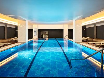 Moderner Innenpool mit blauen Fliesen, Liegestühlen und sanfter Beleuchtung.