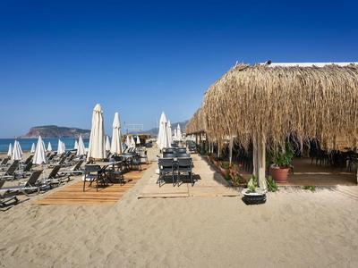 Strand mit Sonnenliegen, weißen Sonnenschirmen und einer Tiki-Bar aus Stroh unter klarem blauem Himmel