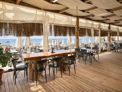 Offenes Restaurant mit Holzboden und Blick aufs Meer bei sonnigem Wetter.