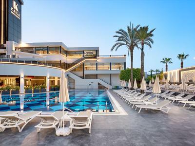 Moderní venkovní bazén s lehátky a palmami vedle hotelové budovy za jasné oblohy.