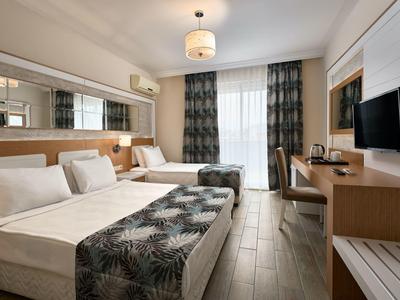 Modernes Hotelzimmer mit zwei Betten, Schreibtisch, TV und großem Fenster mit Vorhängen.