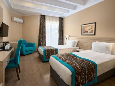 Hotelzimmer mit zwei Einzelbetten, Schreibtisch, Sessel und Fenster mit Vorhängen.