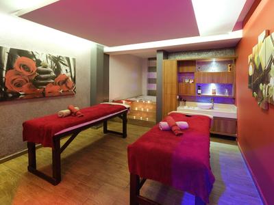 Moderní spa místnost se dvěma masážními stoly, teplým osvětlením a uměleckými díly na stěnách.