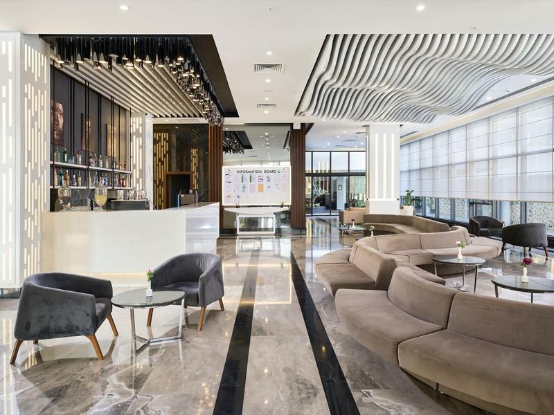 Moderner Hotel-Loungebereich mit eleganten Sesseln, Sofas und großem Fenster mit viel Tageslicht.