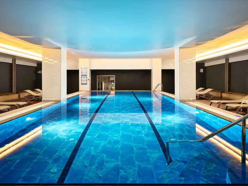 Moderner Innenpool mit blauen Fliesen, Liegestühlen und sanfter Beleuchtung.