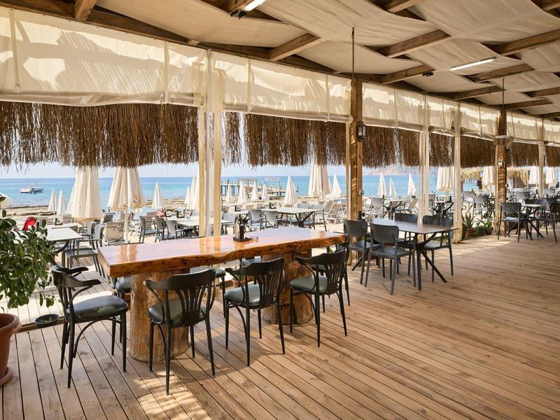 Offenes Restaurant mit Holzboden und Blick aufs Meer bei sonnigem Wetter.