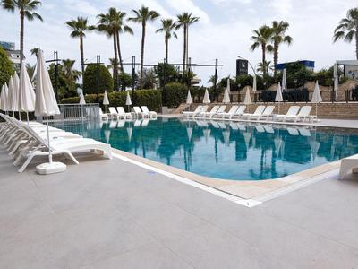 Área de piscina moderna con tumbonas y palmeras en el jardín de un hotel.