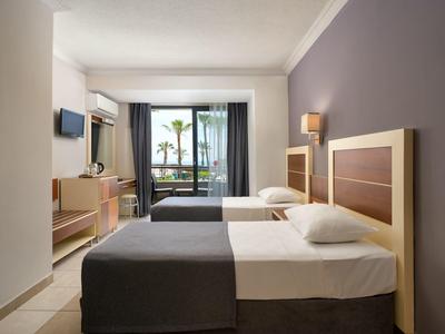 Modern hotel room with two single beds, TV, and balcony overlooking the sea.