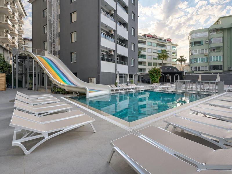 Modern outdoor pool with waterslide, surrounded by white lounge chairs and residential buildings.