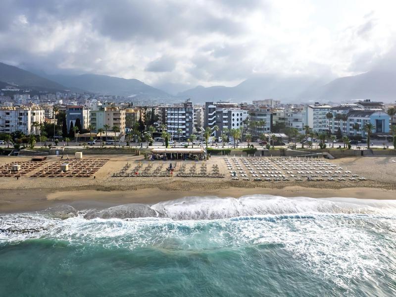 Beach with sun loungers and view of hotels under a cloudy sky.
