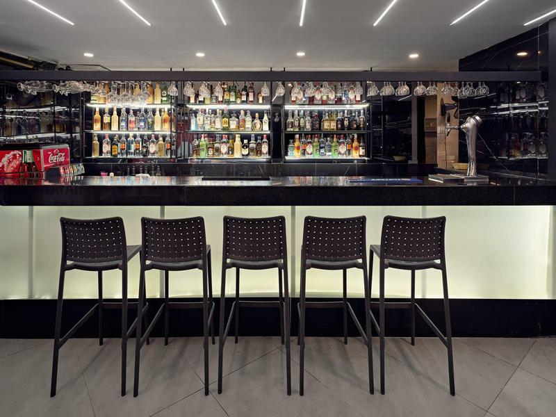Modern hotel bar with five stools in front of illuminated counter and many bottles in the background.