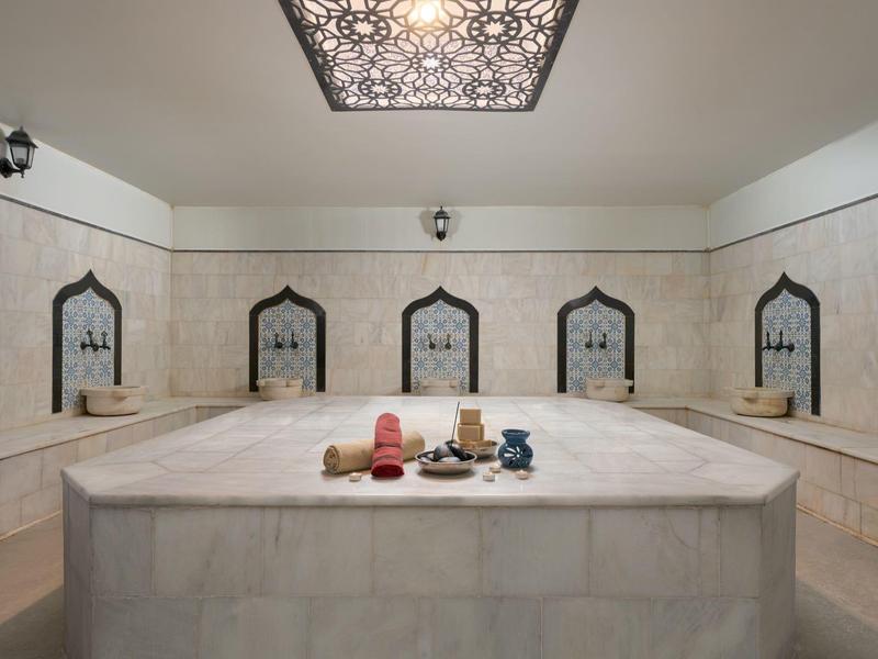 A luxurious marble hammam with five mirrors and decorative ceiling lighting.