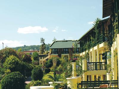 Hotelgebäude mit Balkonen neben einem üppig begrünten Garten unter blauem Himmel.