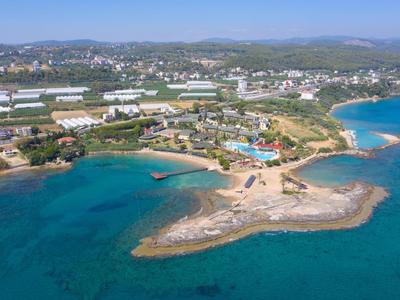 Coastal resort with pools, rocky beach, and buildings near clear blue sea and hills.