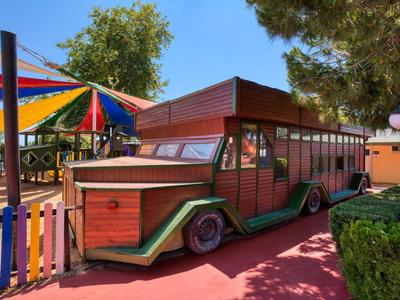 Colorful wooden miniature train ride next to umbrellas and trees in a play area.