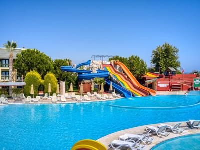 Bright outdoor pool with colorful slides and sun loungers near hotel buildings under clear blue sky.